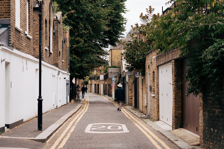 Photograph shows a home relocation scene outside a Hampstead property, with a removal van parked on the pavement near the entrance. Several large cardboard boxes, some wrapped in clear plastic, are st